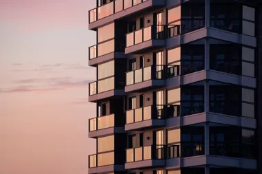 Balkony nowoczesnego apartamentowca oświetlone zachodzącym słońcem na tle różowego nieba.